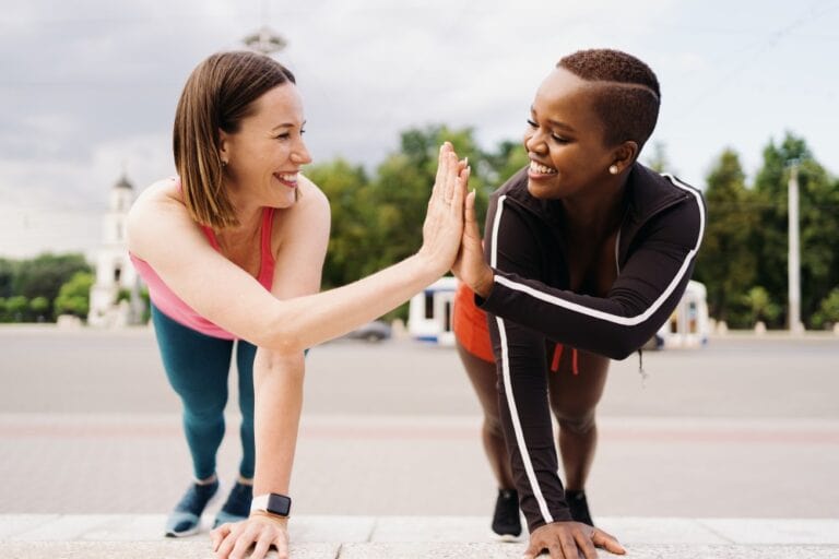 Two women pressing hands together while in plank